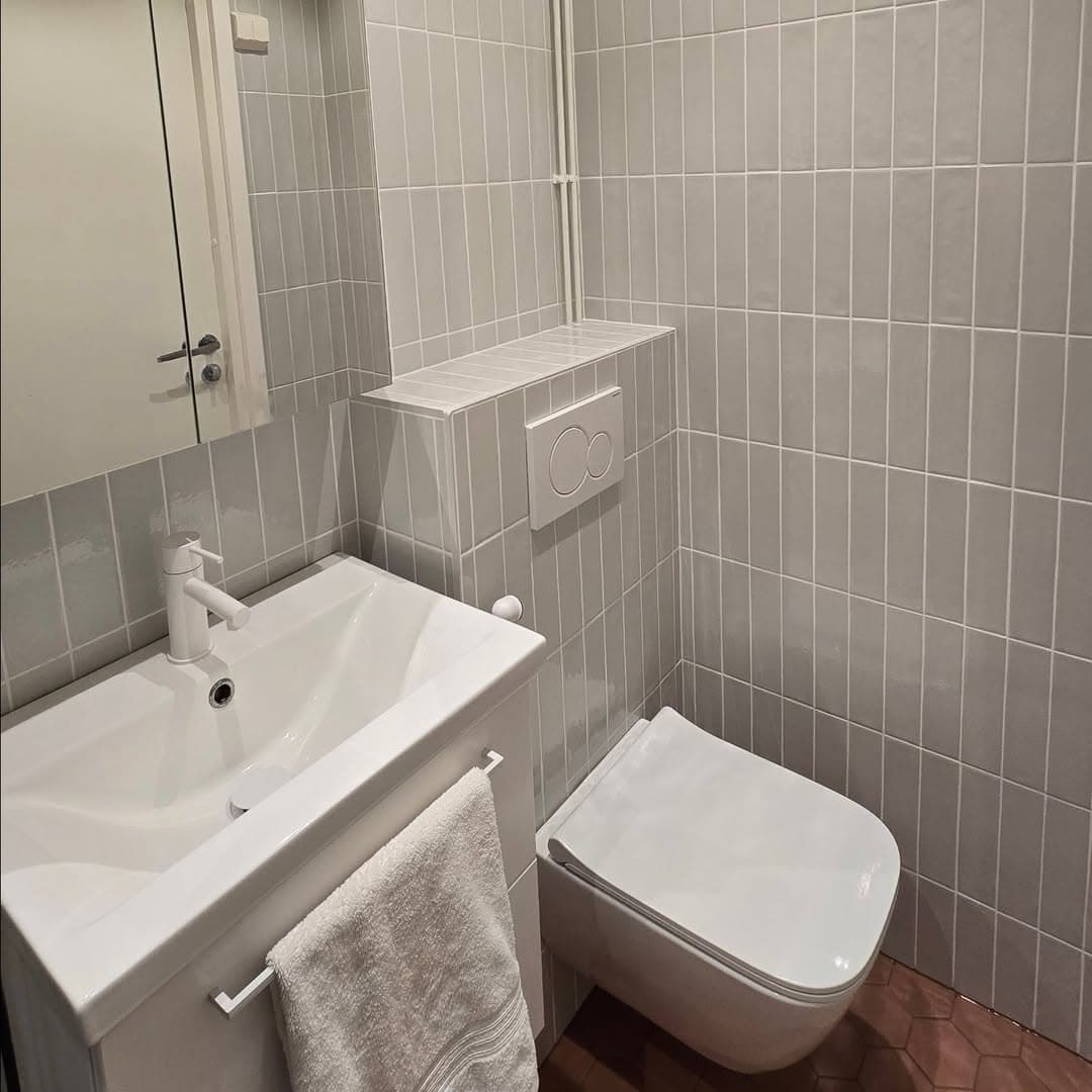 Uudistetun kylpyhuoneen vaalea allas, WC-istuin ja harmaat seinälaatat
